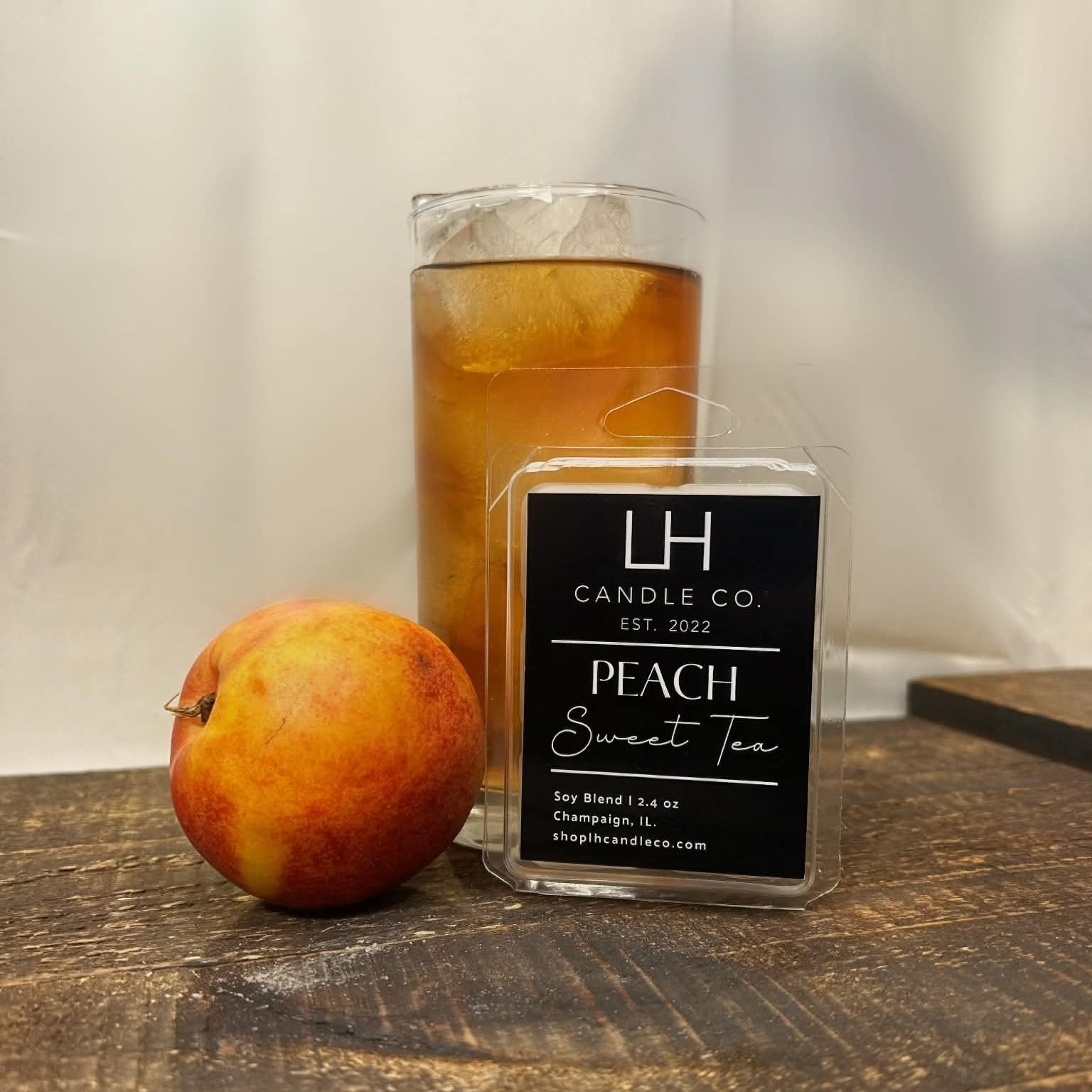 Wax Melt labeled 'LH Candle Co Peach Sweet Tea' next to a peach and a glass of iced tea on a wooden surface.